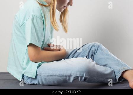 Una bambina di sette anni si siede e tiene il mal di stomaco. Il concetto di digestione impropria dovuta al pancreas, la produzione di enzimi. PA Foto Stock