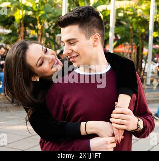 Felice giovane coppia di corse miste che abbraccia e abbraccia con amore e affetto in un parco cittadino indossando abbigliamento casual e sorridendo. Rappresenta una d Foto Stock