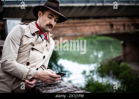 Uomo elegante in un abito retrò che utilizza uno smartphone, con un ponte sullo sfondo Foto Stock