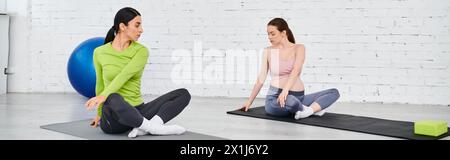 Due donne, una incinta, si siedono serenamente sui tappetini da yoga in un momento condiviso di relax e cameratismo durante un corso per genitori. Foto Stock