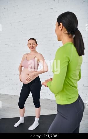 Una donna incinta si trova di fronte a un muro di mattoni bianchi con il suo coach durante un corso per i genitori. Foto Stock