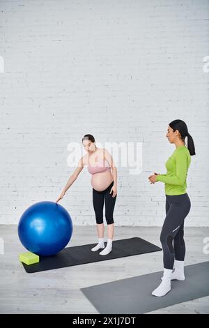 Una donna incinta si trova accanto a una palla blu, esercitando l'equilibrio durante una sessione di allenamento con i genitori. Foto Stock