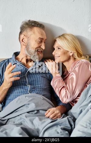 Una coppia matura e amorevole, vestita con intimi indumenti per la casa, che riposano tranquillamente insieme a letto, godendosi l'una con l'altra. Foto Stock