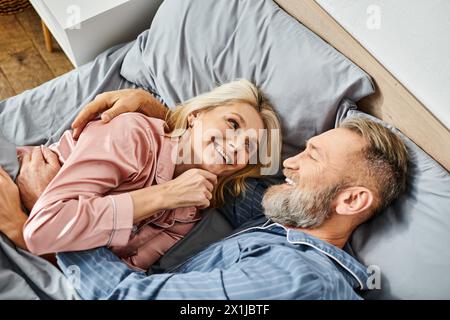 Una coppia matura e amorevole in intimi casalinghi che si stendono insieme su un letto, condividendo un tranquillo momento di intimità e connessione. Foto Stock