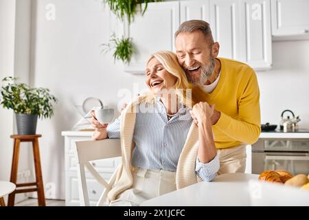 Una coppia matura e amorevole, vestita con intimi indumenti per la casa, condivide un momento di vera risate e gioia nella loro cucina di casa. Foto Stock