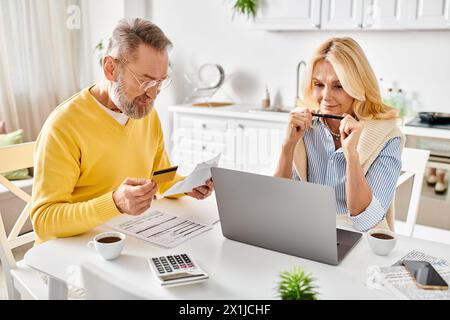 Una coppia matura in intimi costumi da casa, profondamente coinvolta nel rivedere i documenti insieme a un tavolo nella loro cucina. Foto Stock