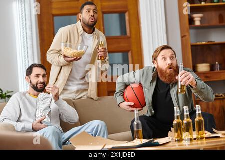 Tre bellissimi uomini interrazziali in un abbigliamento casual che condividono drink, ridono e si divertono insieme a casa. Foto Stock