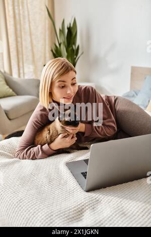 Una donna con i capelli corti si rilassa sul letto, accompagnata dal suo gatto e da un portatile. Foto Stock