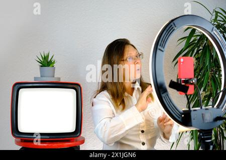Schermo bianco, vecchia TV analogica retrò, donna 45 anni, blogger donna seduta davanti al ring light e smartphone rosso, parla emotivamente sul tema del busin Foto Stock