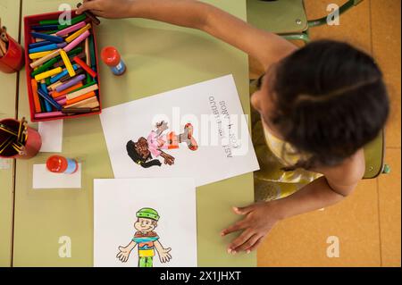 vista dall'alto di una ragazza della scuola elementare dalla pelle scura che disegna con le foto sul suo tavolo della classe a scuola Foto Stock