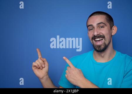 Un uomo adulto sorridente presenta il prodotto, puntando il dito su sfondo blu con spazio di copia. Foto Stock