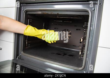 Una ragazza tiene una spugna in mano sullo sfondo di un forno. Concetto per la pulizia dei forni elettrici in cucina. azienda di pulizie Foto Stock