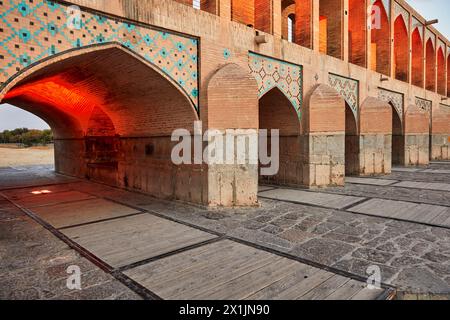 Vista degli archi a volta illuminati del Ponte Khaju del XVII secolo sul fiume Zayanderud durante la stagione secca con letto asciutto. Isfahan, Iran. Foto Stock