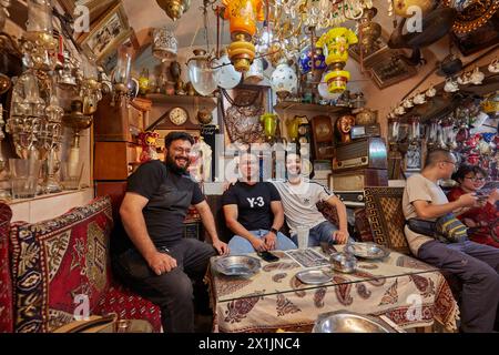 Compagnia di giovani uomini iraniani sorridenti seduti insieme all'Azadegan Cafe con la sua insolita decorazione interna. Grand Bazaar, Isfahan, Iran. Foto Stock