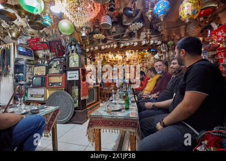 Gli uomini iraniani siedono insieme ad un piccolo tavolo nell'Azadegan Cafe con la sua insolita decorazione interna. Grand Bazaar, Isfahan, Iran. Foto Stock