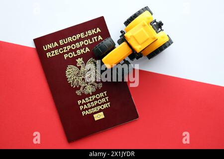 Passaporto rosso polacco e trattore giallo su una bandiera bianca e rossa liscia della Polonia Foto Stock