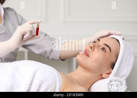 Cosmetologo professionista che tiene in mano una fiala per la cura della pelle mentre lavora con il cliente in clinica, primo piano Foto Stock