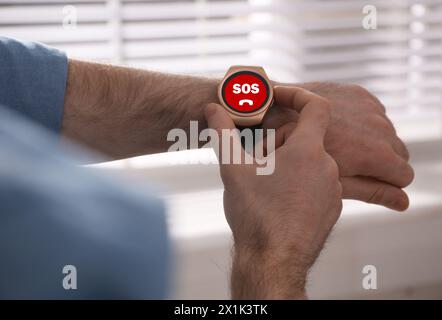 Uomo che utilizza la funzione SOS su uno smartwatch in interni, primo piano Foto Stock