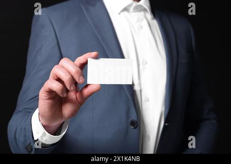 Uomo d'affari che tiene un biglietto da visita vuoto su sfondo nero, primo piano Foto Stock