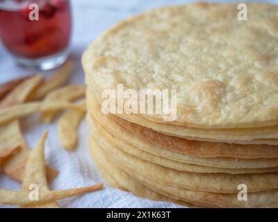 Una pila di sottili strati di burro rotondi al forno, frammenti di impasto su un asciugamano bianco pronto per preparare la pasta sfoglia a pasta frolla Napoleone. Vetro rosso dietro. Foto Stock