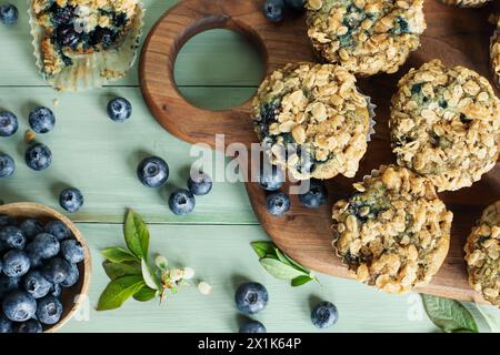 Muffin ai mirtilli freschi con condimento di avena e mirtilli crudi che fuoriescono da un cucchiaio di legno. Vista dal piano d'esame con sfondo sfocato. Foto Stock