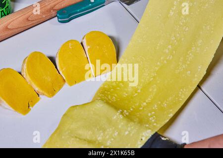 Foglio di pasta giallo brillante e spicchi di impasto sul tagliere, vista rialzata Foto Stock