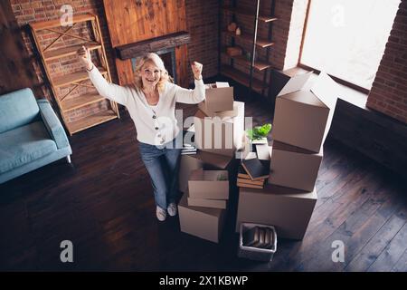 Ritratto a grandezza naturale della signora anziana alzare i pugni di successo indossa cardigan bianco loft interno casa interna Foto Stock