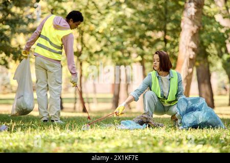 Una coppia socialmente attiva e diversificata di giubbotti di sicurezza e guanti che puliscono l'erba in un parco. Foto Stock