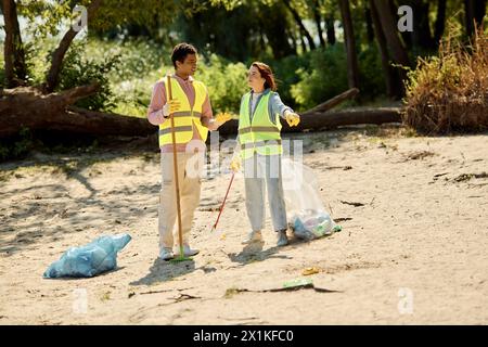 Un uomo e una donna, una coppia socialmente attiva e diversificata, puliscono una spiaggia indossando giubbotti di sicurezza e guanti. Foto Stock