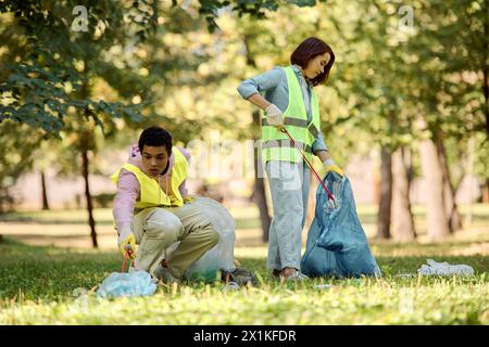 Una coppia socialmente attiva e diversificata con giubbotti di sicurezza e guanti che puliscono diligentemente l'erba in un parco. Foto Stock