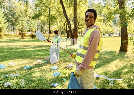 Coppia socialmente attiva e diversificata con giubbotti di sicurezza e guanti che puliscono un parco Foto Stock