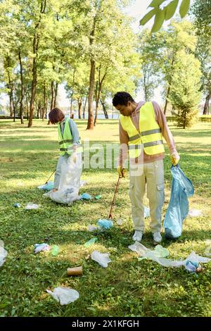 Una coppia socialmente attiva e diversificata di giubbotti di sicurezza e guanti che puliscono insieme un parco, appassionata di conservazione ambientale. Foto Stock