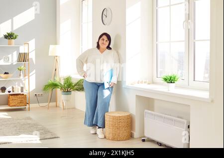 Giovane donna in sovrappeso con abiti casual in piedi a parete appoggiata Foto Stock