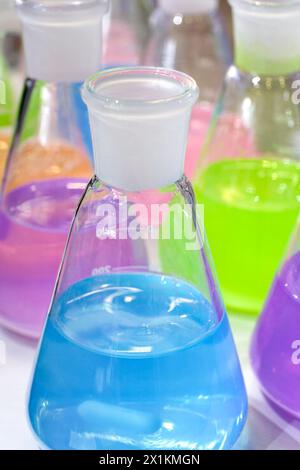 Liquidi multicolore in matracci conici da laboratorio chimico, primo piano, messa a fuoco selettiva, background chimico astratto Foto Stock