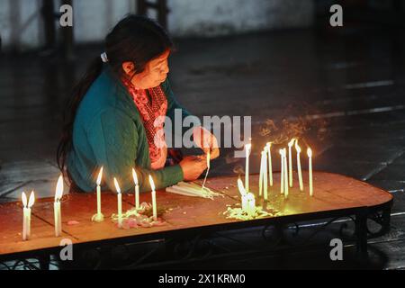 Una donna indigena maya prega e brucia candele su una piattaforma d'altare all'interno della chiesa cattolica Inglesia de Santo Tomas del XV secolo a Chichicastenango, Guatemala. La Chiesa cattolica e le credenze maya si mescolarono molto tempo fa nelle regioni indigene del Guatemala in un processo chiamato sincretismo. Foto Stock