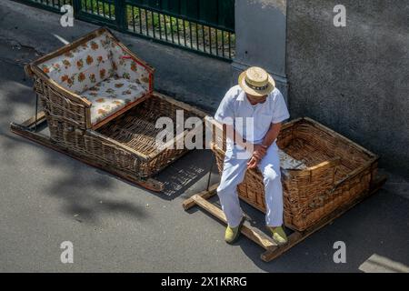 Uomo che indossa una barca di paglia seduto su una tradizionale slitta con cesti di vimini a Monte Funchal, isola di Madeira, Portogallo Foto Stock