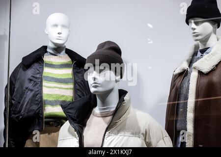 Tre manichini con eleganti maglioni invernali e cappelli in pelliccia sintetica in vetrina. La bretella di fissaggio aggiunge un tocco di tendenza al tuo look Foto Stock