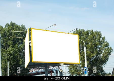 Un cartellone bianco rettangolare si erge alto su uno sfondo di alberi e cielo, mostrando vibrante erba verde e soffici nuvole Foto Stock