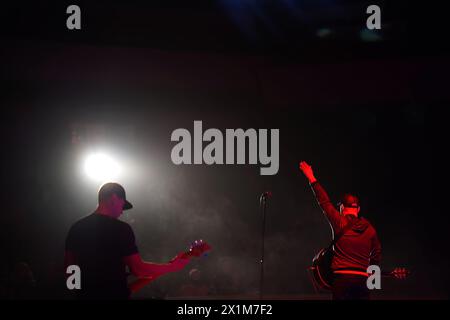 Silhouette cantante della rock band con la chitarra che canta al microfono con le mani alzate in rosso durante il concerto Foto Stock