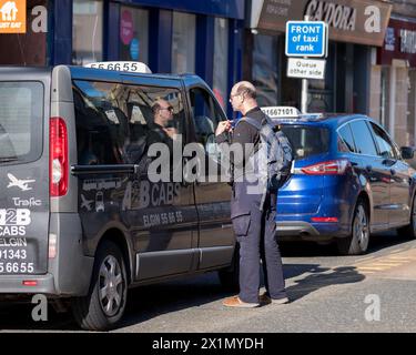 17 aprile 2024. Elgin, Moray, Scozia. Si tratta di un uomo che parla con un tassista che è seduto nel suo taxi e in una classifica dei taxi su High Street. Foto Stock