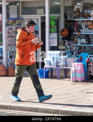 17 aprile 2024. Elgin, Moray, Scozia. Questo è un giovane che cammina lungo la strada principale di Elgin e mangia un cono di patatine. Foto Stock