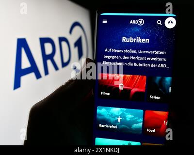 Persona che detiene un cellulare con la pagina web dell’organismo tedesco di radiodiffusione pubblica ARD davanti al logo. Messa a fuoco al centro del display del telefono. Foto Stock