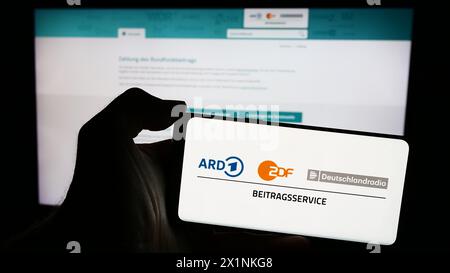 Persona che possiede un telefono cellulare con il logo di ARD ZDF Deutschlandradio Beitragsservice davanti alla pagina web. Mettere a fuoco il display del telefono. Foto Stock