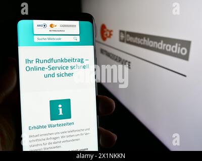 Persona che possiede un telefono cellulare con pagina web di ARD ZDF Deutschlandradio Beitragsservice davanti al logo. Messa a fuoco al centro del display del telefono. Foto Stock