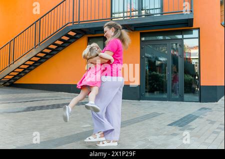 Madre felice che oscilla e gira una figlia carina in cerchio accanto alle braccia all'aperto. Bambino giocoso energico e gioioso che si diverte mentre si lega con la mamma Foto Stock