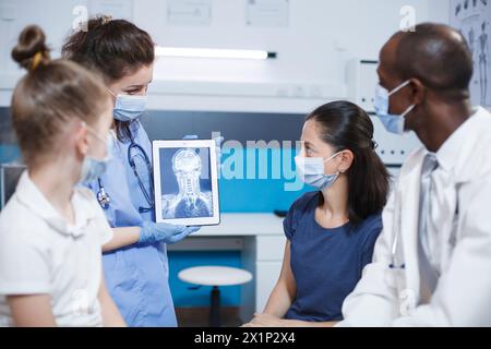 Il medico analizza una scansione cerebrale mentre spiega i risultati, in una clinica moderna con tecnologia all'avanguardia. Infermiere che tiene in mano un tablet che visualizza un'immagine radiografica della testa di un paziente. Foto Stock