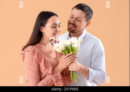 Felice giovane coppia con tulipani su sfondo beige Foto Stock