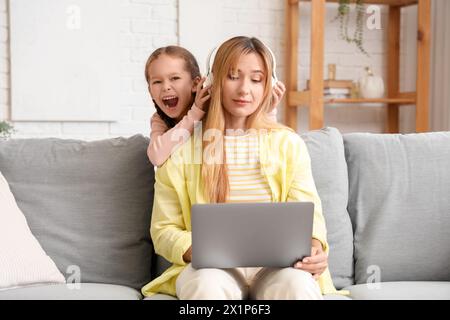 Una giovane donna che lavora con le cuffie stressava la sua figlioletta rumorosa a casa Foto Stock