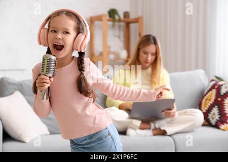 Bambina rumorosa in cuffie con microfono che canta a casa Foto Stock