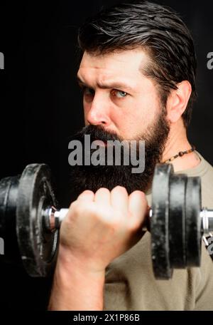 Sollevamento pesi e bodybuilding. Ritratto ravvicinato di un muscoloso sportivo barbuto che solleva il manubrio. Un bodybuilder sportivo forte che pompa i muscoli con Foto Stock